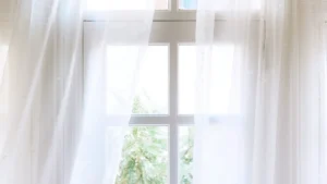 Clean, sheer white curtains framing a bright window with green leaves outside