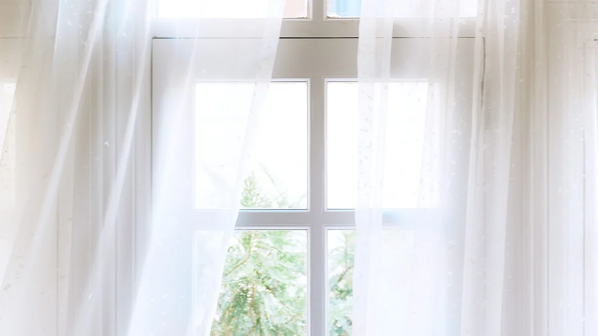 Clean, sheer white curtains framing a bright window with green leaves outside