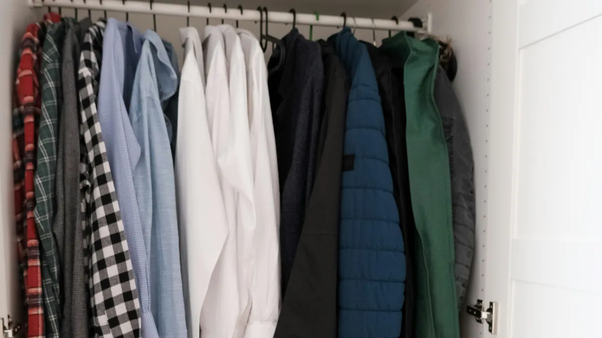 Neat white closet with shirts, jackets, and a green garment bag on hangers